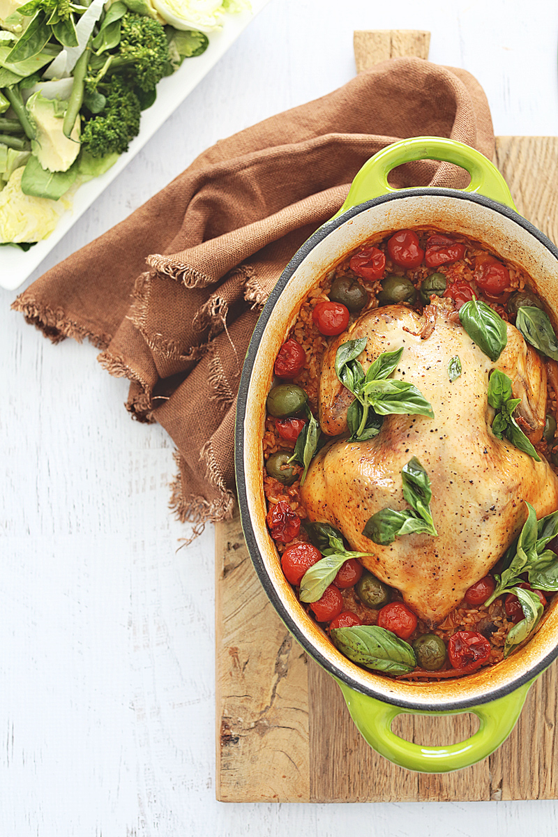 A whole roasted chicken with cherry tomatoes, olives and fresh basil, served with steamed greens